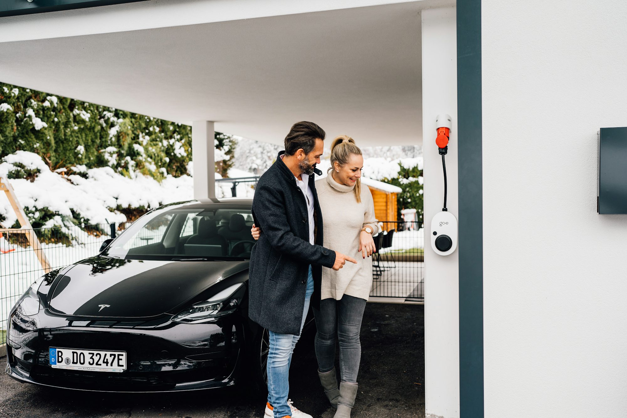 A couple standing beside their electric car while it charges at home