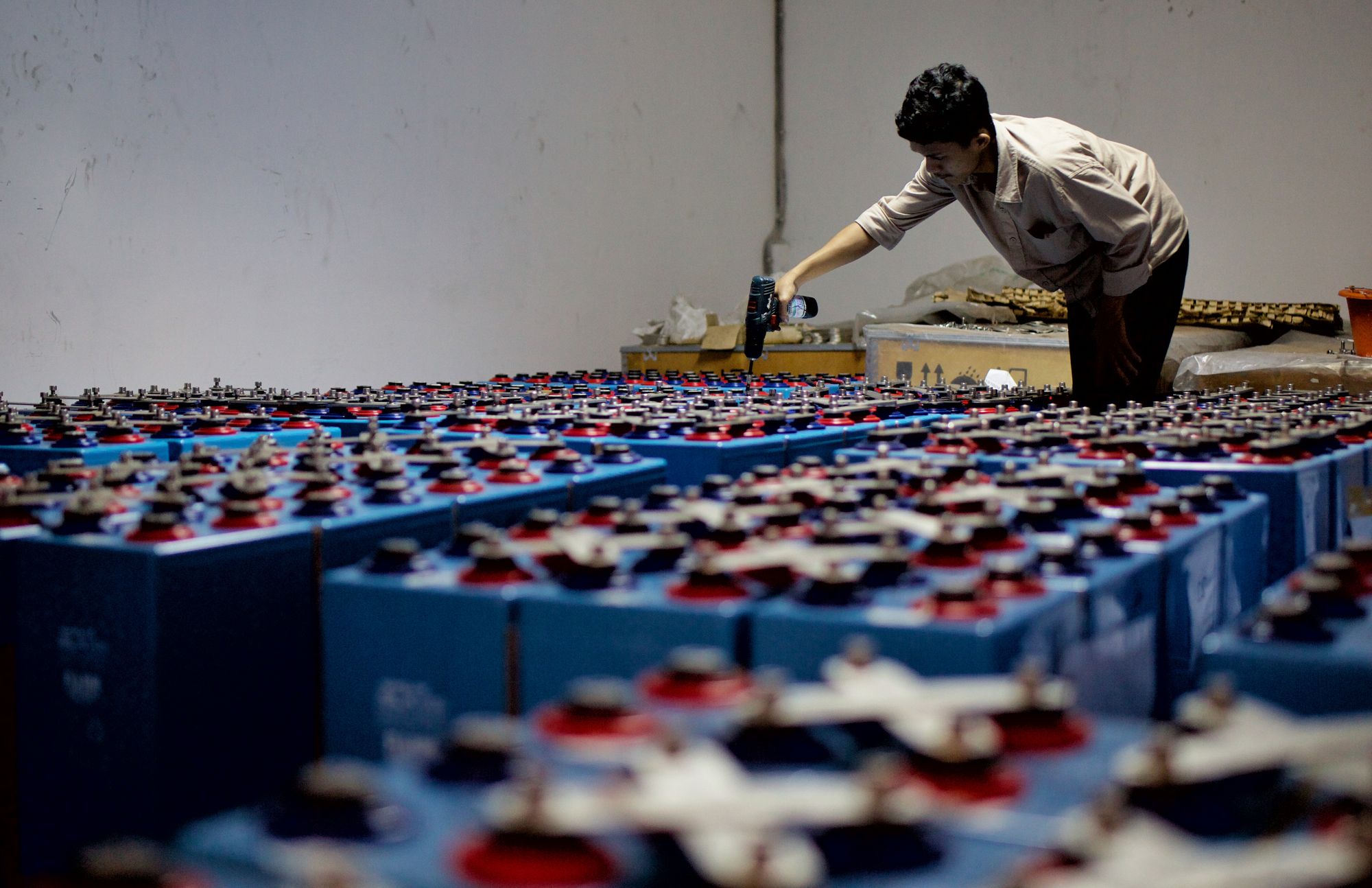 A worker in a facility inspecting rows of industrial battery cells during a quality check