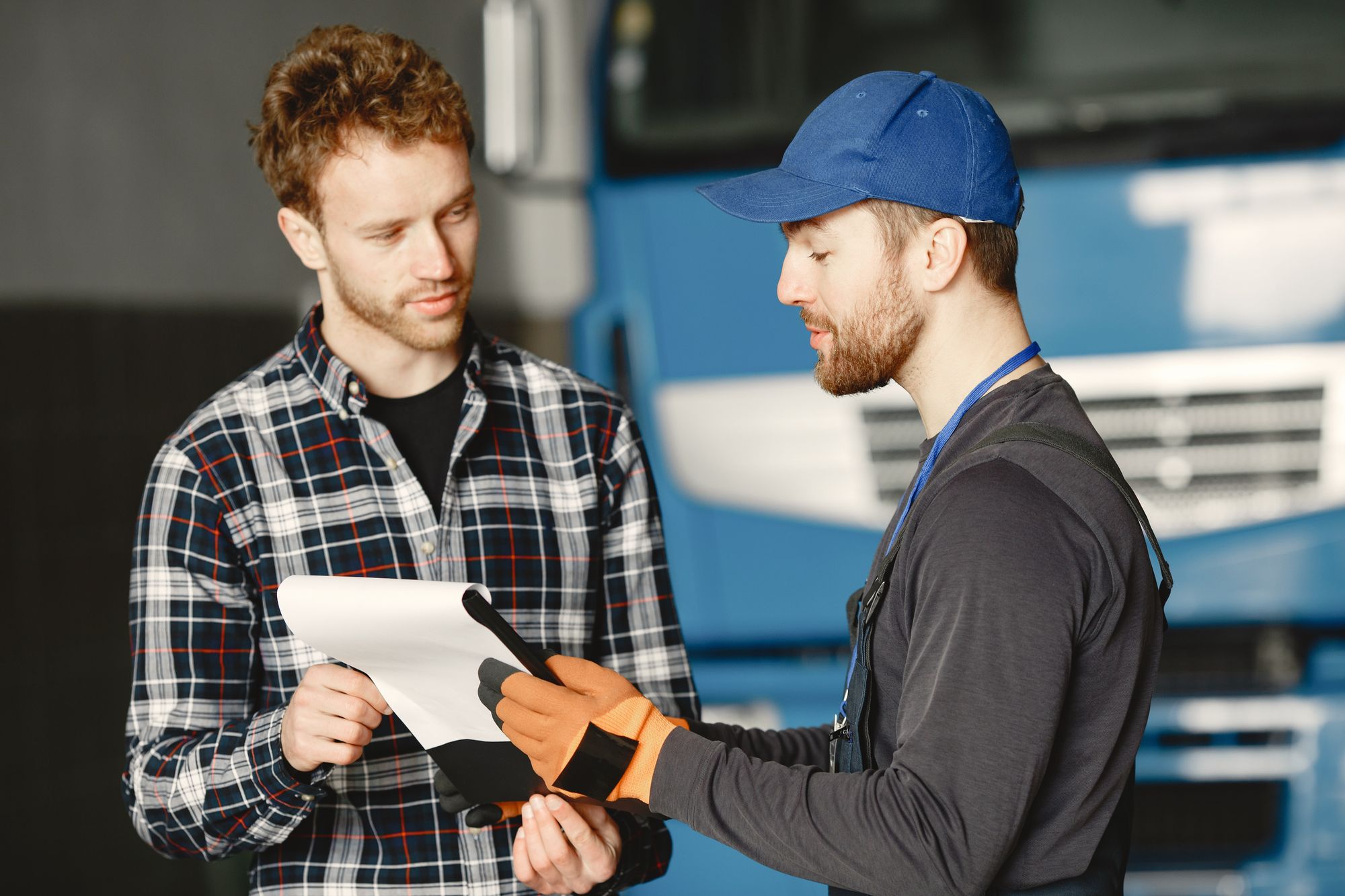 A mechanic in uniform talking with a customer about vehicle maintenance inside a garage