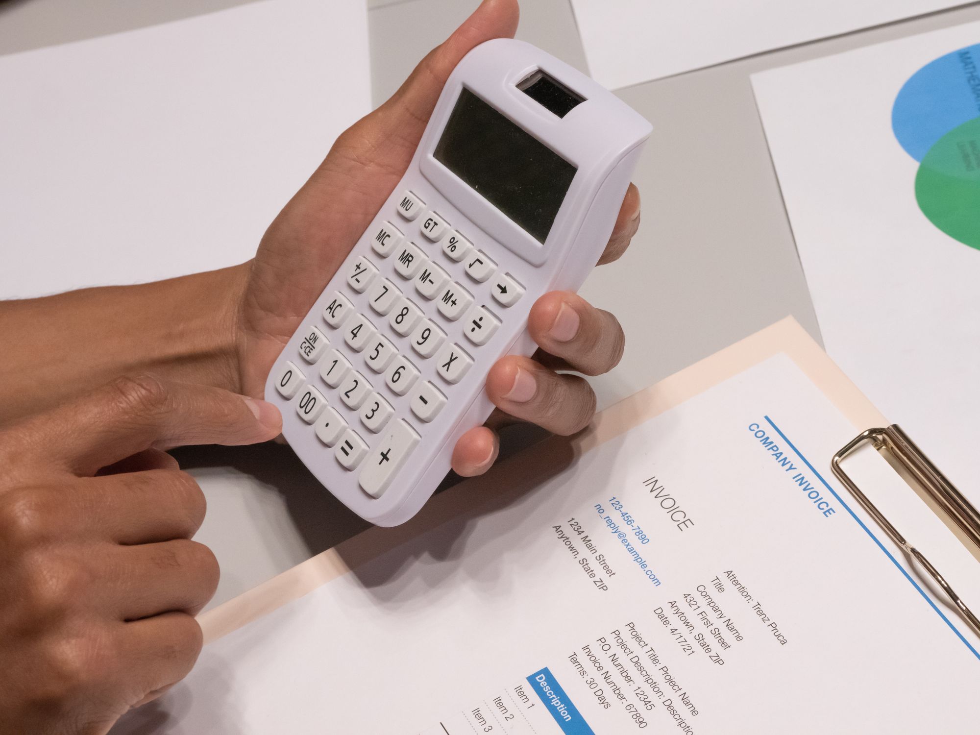 Close-up of a pair of hands working a calculator next to a printed invoice