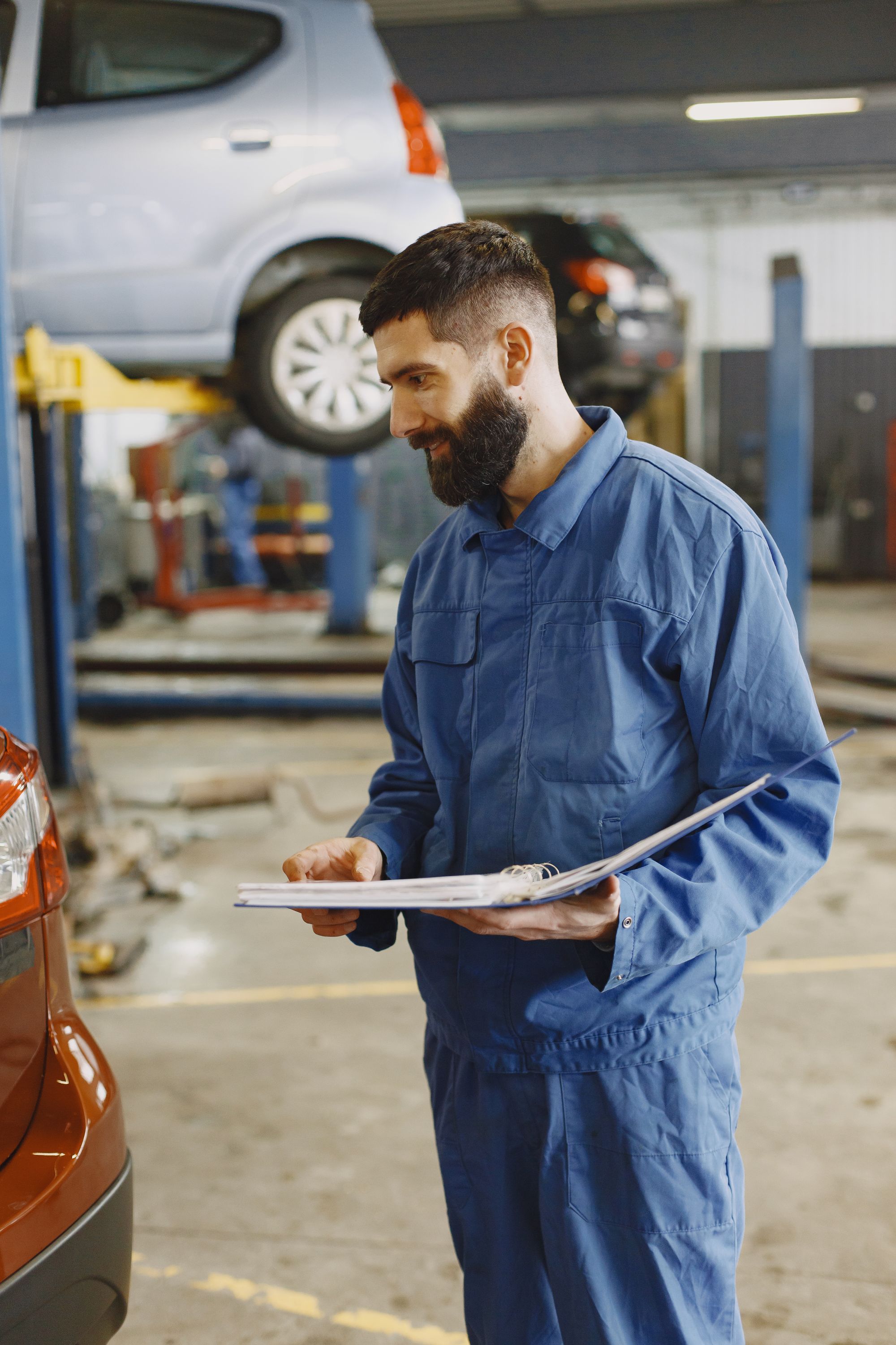 A mechanic in blue coveralls reading through paperwork in an auto repair workshop